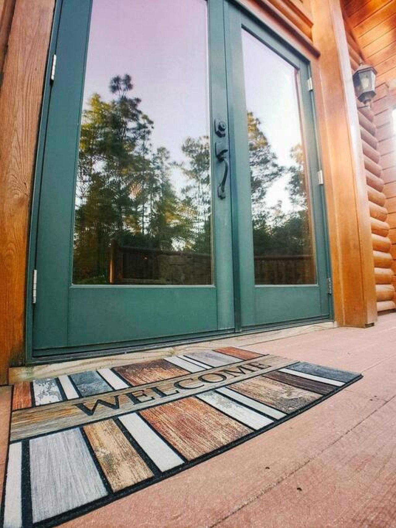 A wooden exterior with a green door and a welcome mat.