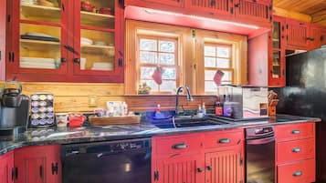 Une cuisine avec des meubles de couleur rouge, un lave-vaisselle noir et une fenêtre ornée de rideaux à carreaux.