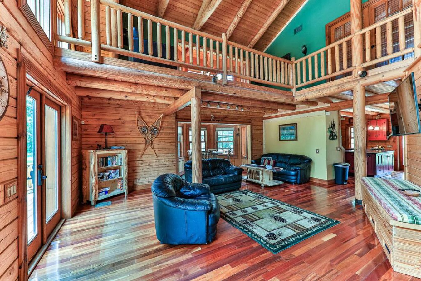 A spacious log cabin interior with a loft bedroom, a living room with leather sofas, and a dining area.
