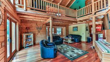 A spacious log cabin interior with a loft bedroom, a living room with leather sofas, and a dining area.