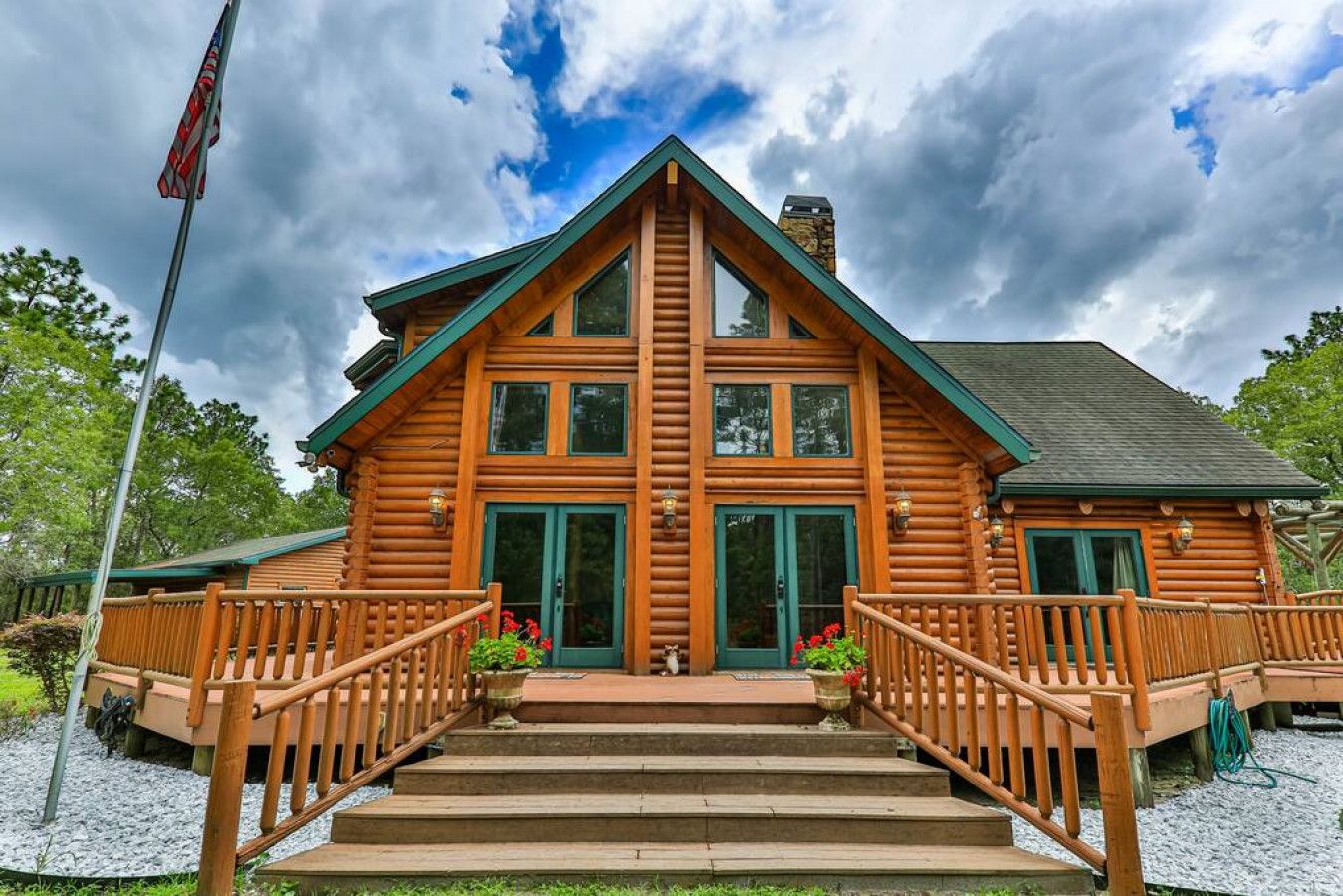 A log cabin with a front porch, a chimney, and a flagpole.