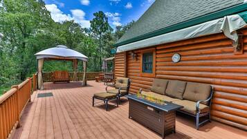 A wooden deck with outdoor furniture, a covered seating area, and a log cabin structure.