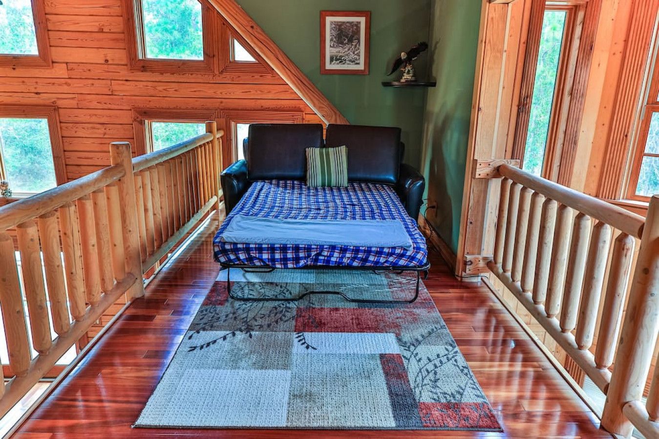 A wooden cabin room with a bed, a window, and a wooden railing.