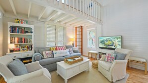A spacious living room with a high ceiling, a white staircase, a bookshelf, a grey sofa, a white coffee table, and a television. - Just 5 Houses to Beach in Seaside! Sleeps Six + 2 Adult Bikes! (Santa Rosa Beach)