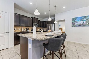 A modern kitchen with dark cabinets, a granite countertop, and a central island with bar stools. - Spacious 5BR Home with Private Pool in Kissimmee (Kissimmee)