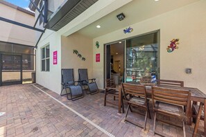 An outdoor patio area with a brick floor, wooden tables and chairs, and a glass door entrance.