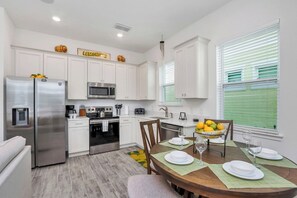 A modern kitchen with white cabinetry, stainless steel appliances, and a dining area with a wooden table set for four.