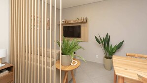 A modern living room with a sofa, a round wooden table with a potted plant, a wooden dining table, and a sliding glass door. - 360 Av. Ipiranga (São Paulo)