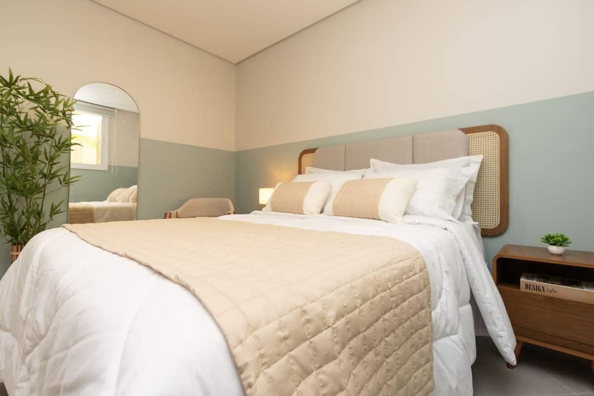 Une chambre à coucher bien rangée, avec un grand lit, une table de chevet avec une lampe, un miroir et une petite plante posée sur la table de chevet.