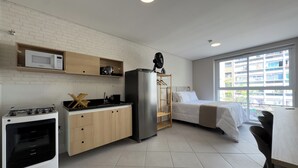 A compact hotel room with a kitchenette, a bed, a bedside table, and a window with a view of buildings. - 360 Av. Ipiranga (São Paulo)