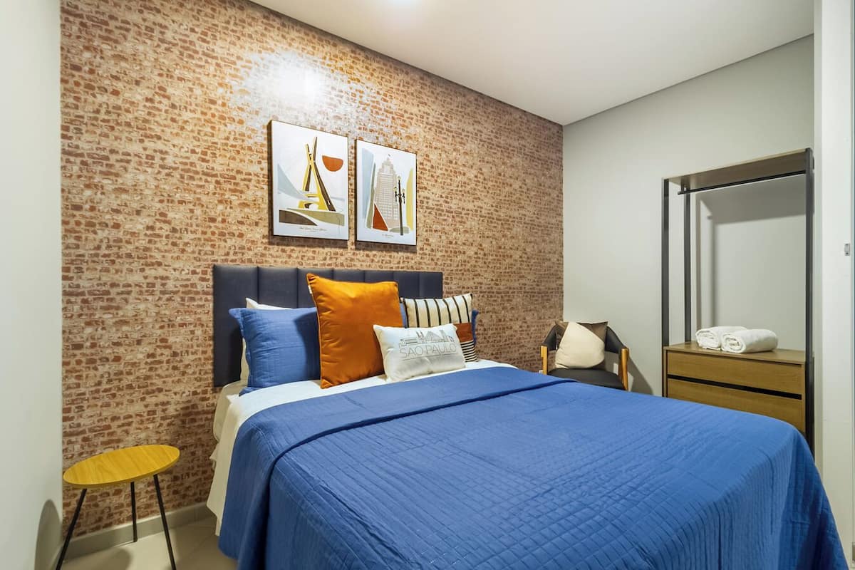 Une chambre d’hôtel avec un mur décoré d’un motif en briques, un lit avec une literie bleue, une table de chevet en bois, une chaise et un miroir.