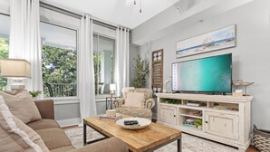 A living room with a sofa, coffee table, TV, and a white cabinet with shelves. - 1BR Condo at Baytowne! Steps to Wharf, Tropical Pool & Hot Tub, Balcony View. (Miramar Beach)