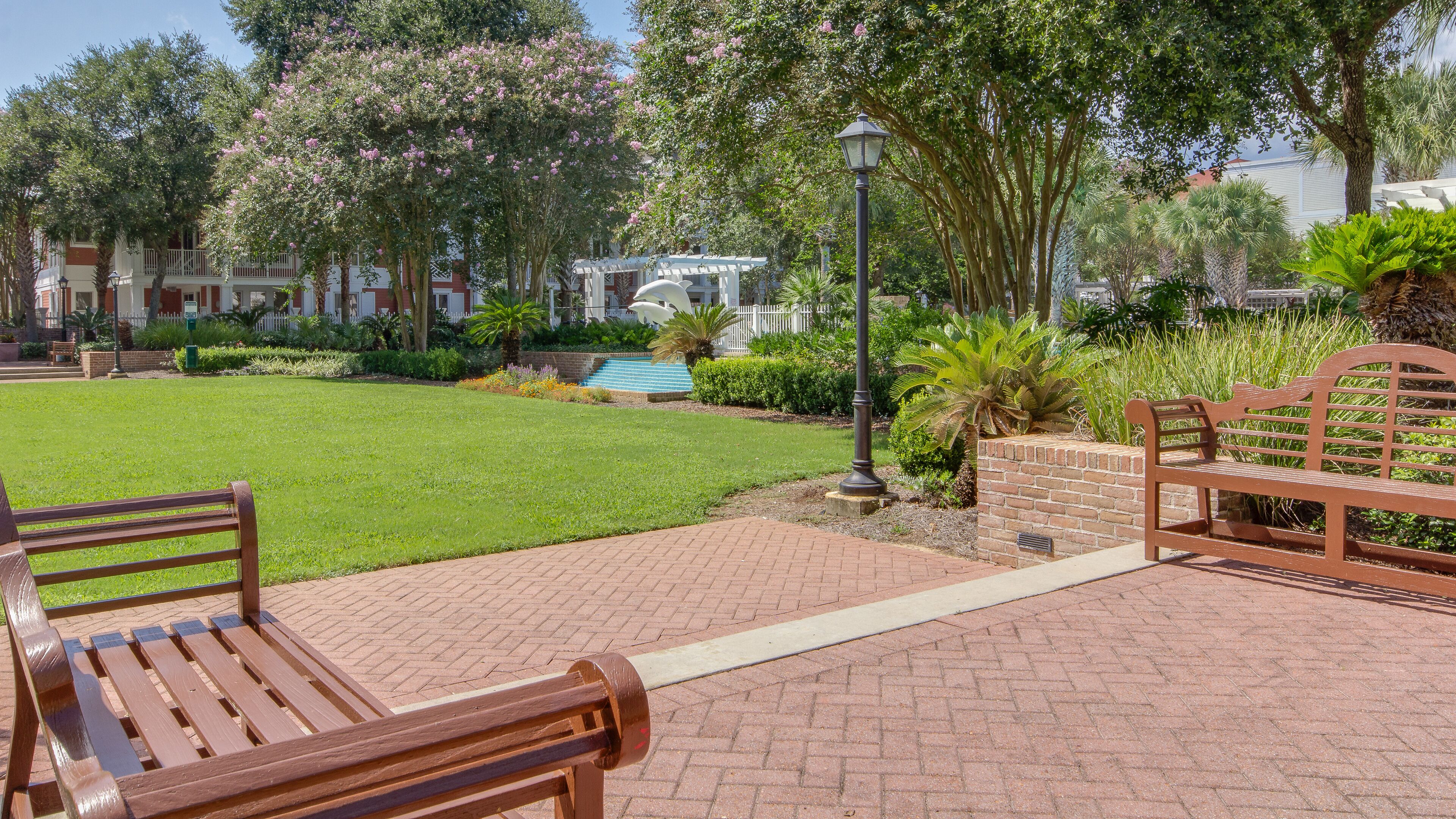 A courtyard with a lawn, benches, a brick pathway, and a pool area.