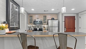 A modern kitchen with stainless steel appliances, wooden cabinets, and a central island with bar stools. - 1BR Condo at Baytowne! Steps to Wharf, Tropical Pool & Hot Tub, Balcony View. (Miramar Beach)