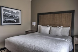 A neatly made bed with a large headboard, a bedside lamp, and a framed picture of a mountain landscape on the wall. - Best Western Plus Kalispell/glacier Park West Hote (Kalispell)