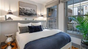 Quarto com cama, luminárias de cabeceira, quadro emoldurado e janela com vista para o exterior.