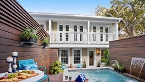Uma casa de dois andares com piscina, mesa de jantar com comida e área de estar externa.