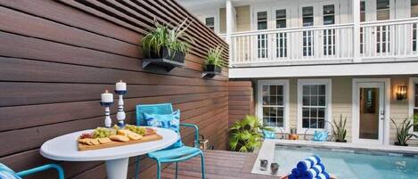 Zona de piscina con terraza de madera, una mesa con una bandeja de frutas y sillas azules.