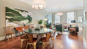 Un salon spacieux avec une table de salle à manger ronde, des sièges confortables et un grand tableau abstrait accroché au mur.