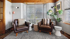 A cozy room with two leather armchairs, a small round table, a potted plant, and a window with blinds. - Bendalong | Rural Retreat, Short Drive to CBD (Nashdale)