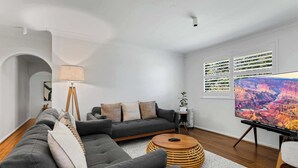 A modern living room with a sectional sofa, a standing lamp, a large flat-screen TV, and a window with a view of the Grand Canyon. - Bendalong | Rural Retreat, Short Drive to CBD (Nashdale)