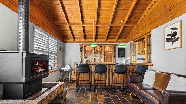 A cozy interior with a fireplace, wooden ceiling, stone flooring, a bar area, and a leather sofa. - Bendalong | Rural Retreat, Short Drive to CBD (Nashdale)