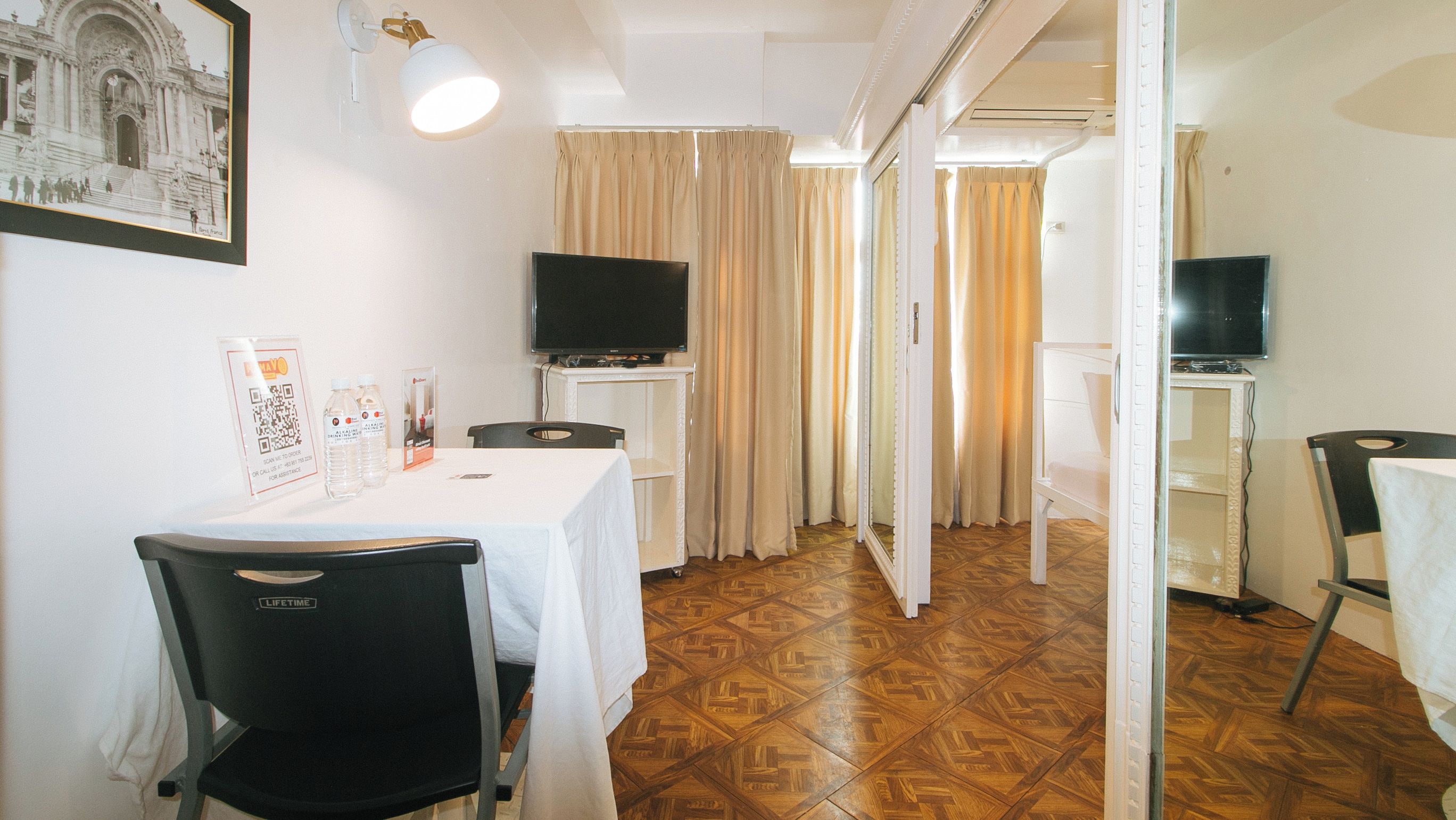 Quarto de hotel com área de refeições, televisão e corredor que dá para outro quarto.
