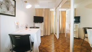 Habitación de hotel con zona de comedor, televisor y un pasillo que lleva a otra habitación.