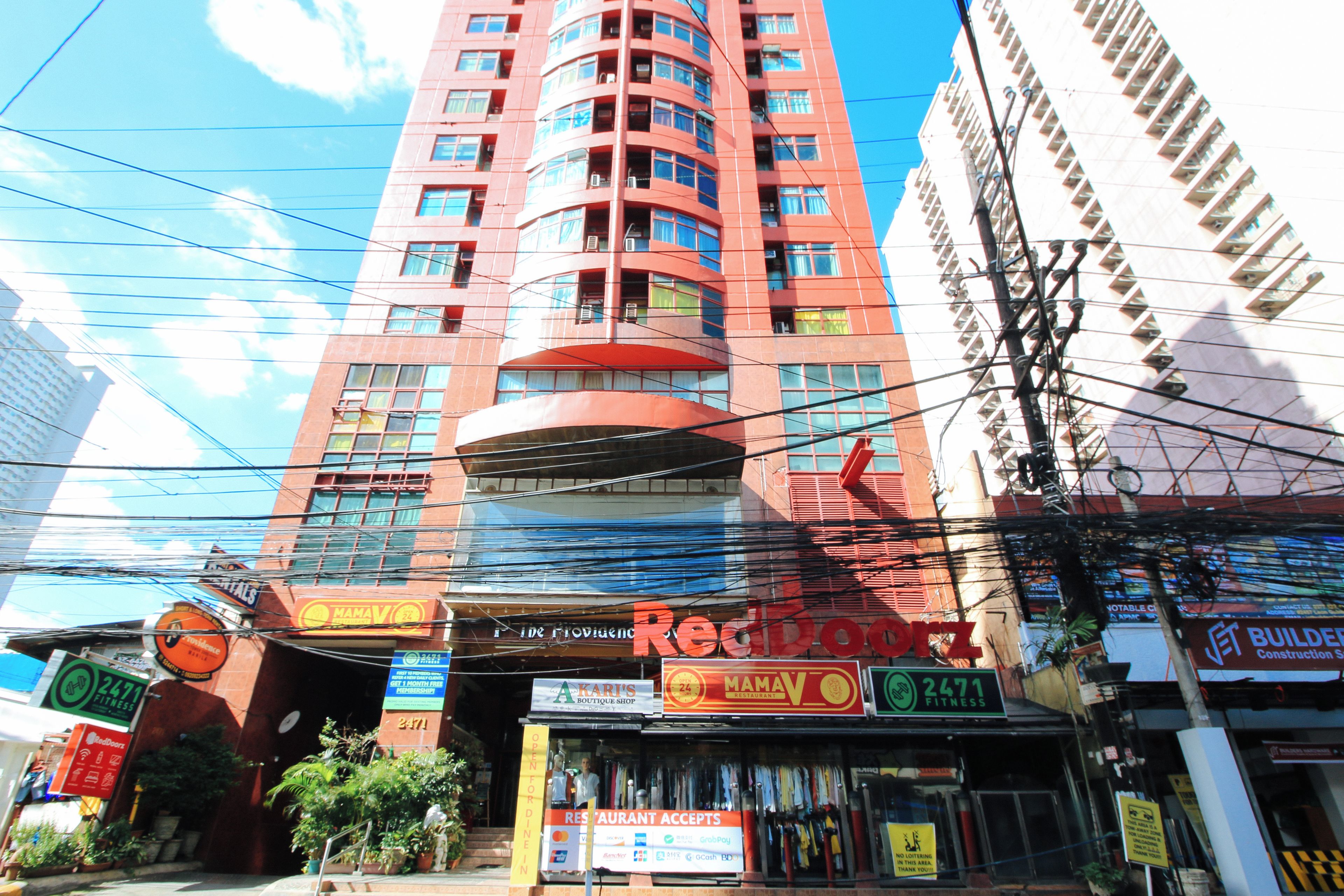 Um edifício com vários andares e diversos estabelecimentos comerciais no andar térreo, incluindo um centro de fitness e um restaurante.