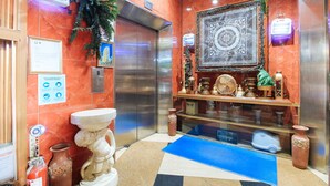 An elevator with a marble wall, a framed picture, a small Christmas tree, and a decorative shelf with various items. - Reddoorz @ The Providence Tower (Manila)