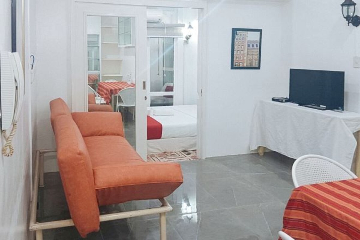 A hotel room with a bed, a sofa, a television, and a table with a white tablecloth.