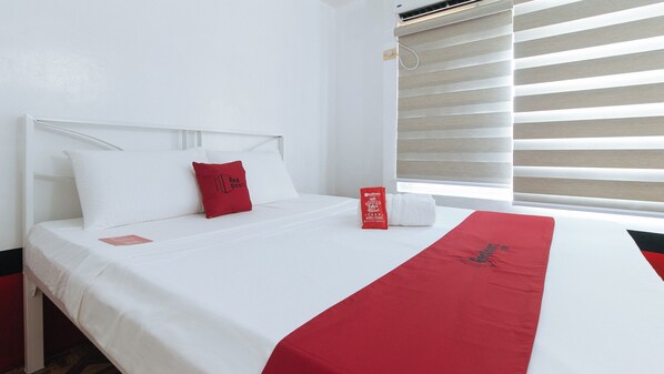 Quarto de hotel com cama, travesseiro vermelho, manta vermelha e janela com persianas.
