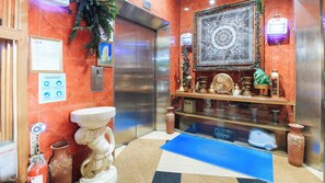 An elevator with a marble wall, a framed picture, a small Christmas tree, and a decorative shelf with various items. - Reddoorz @ The Providence Tower (Manila)
