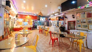 A restaurant interior with round tables and chairs, a counter with food items, and a TV screen displaying content. - Reddoorz @ The Providence Tower (Manila)