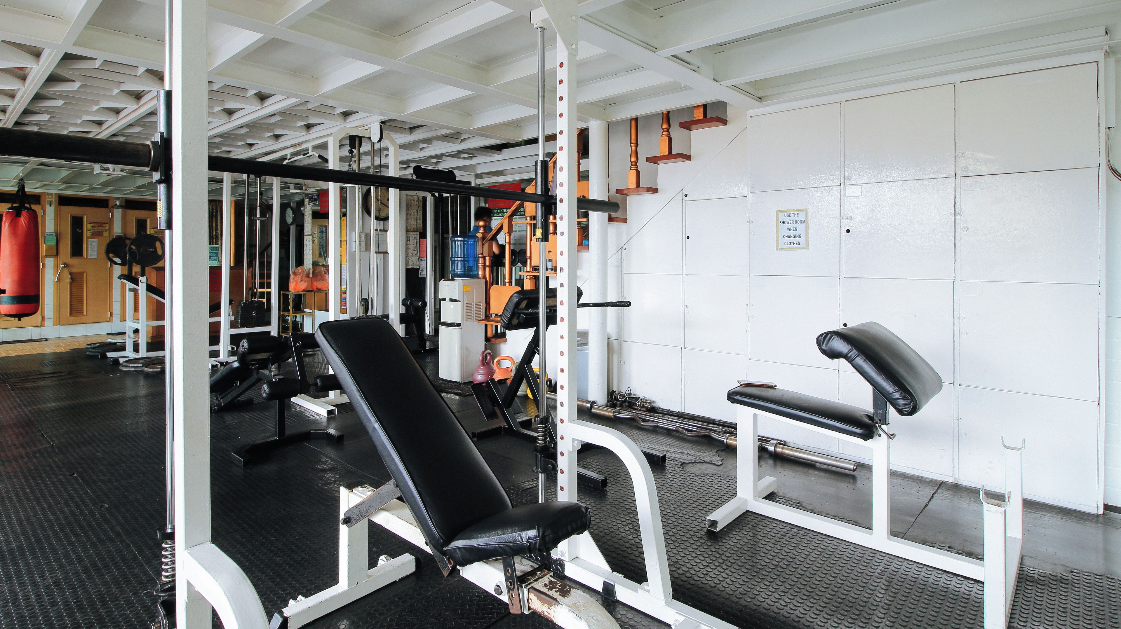 Academia com equipamentos de musculação, bancos e espelho.