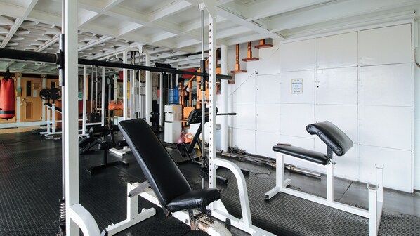 Un gimnasio con equipo de levantamiento de pesas, bancos y un espejo grande.