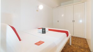 Quarto individual com uma colcha branca, detalhes em vermelho, toalha RedDoorz e um guarda-roupa.