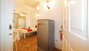 A small room with a bed, a refrigerator, a window with blinds, and a wall-mounted light fixture. - Reddoorz @ The Providence Tower (Manila)
