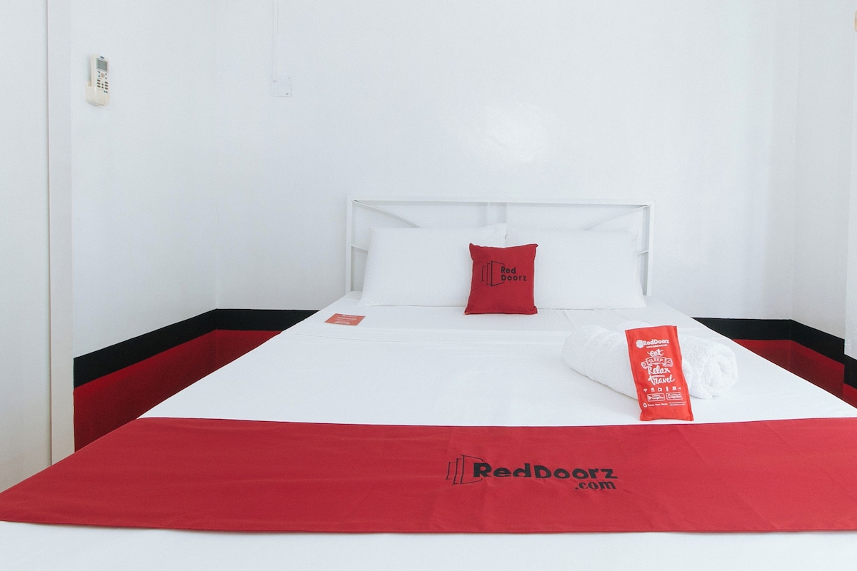 A neatly made bed with a red and white bedspread, a red pillow, and a red towel with text.