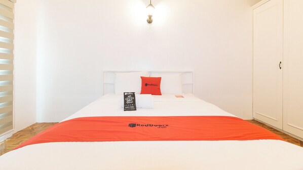 A hotel room with a bed, a red pillow, a white headboard, a red blanket, and a RedDoorz branded pillow. - Reddoorz @ The Providence Tower (Manila)
