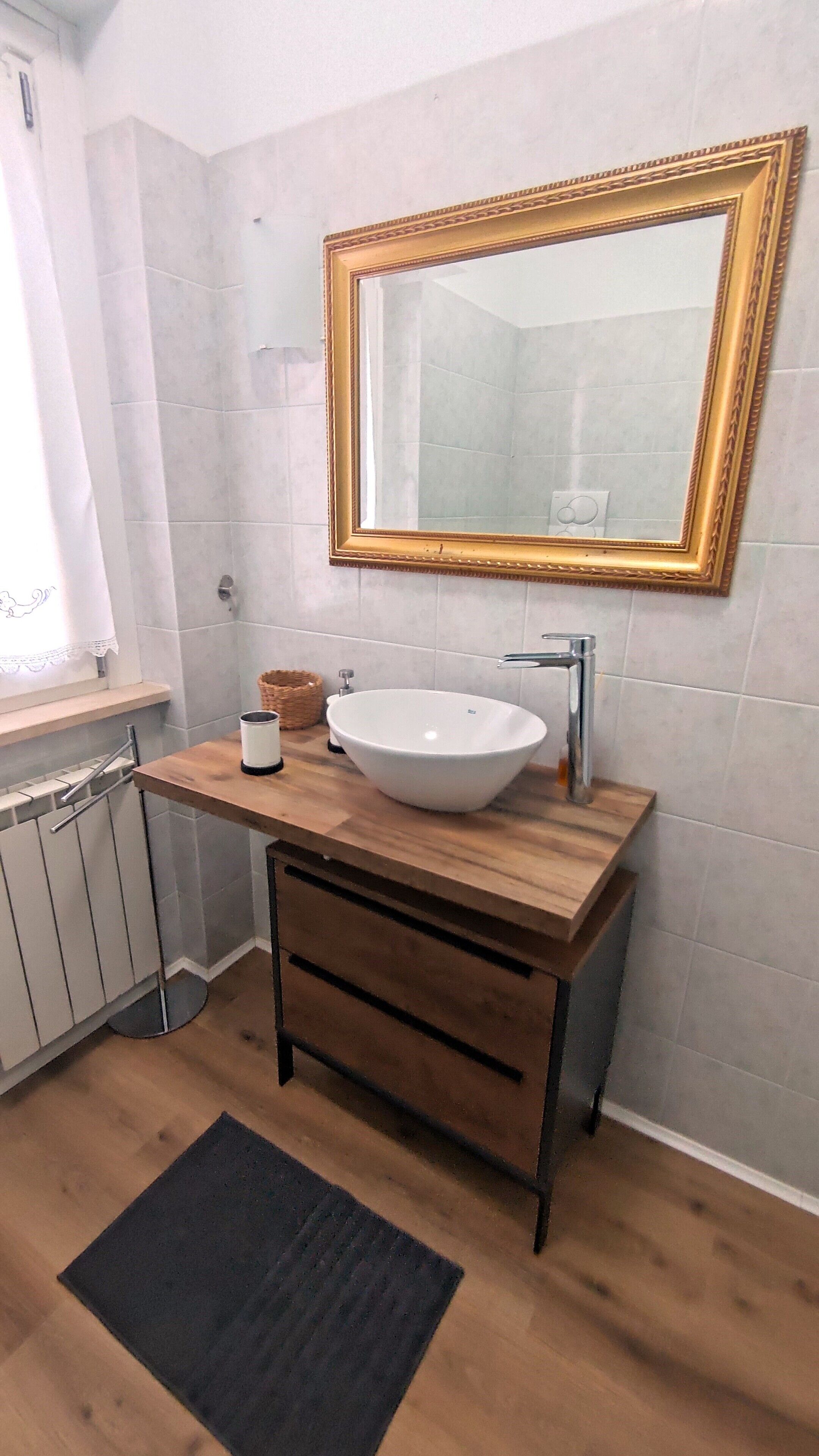A bathroom with a white sink, wooden vanity, and a large mirror with a gold frame.