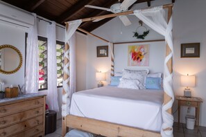 Quarto com cama de madeira, dossel branco, ventoinha no teto, abajures e espelho no penteadeira.