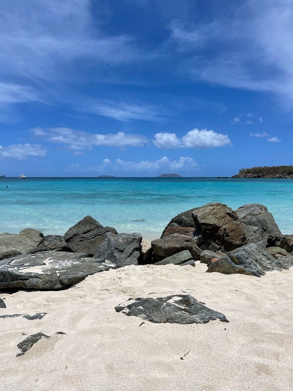 Uma praia com águas turquesa cristalinas, grandes rochas em primeiro plano e uma ilha ao longe.