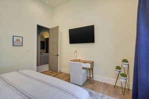 A bedroom with a bed, a desk, a TV, and a small potted plant.