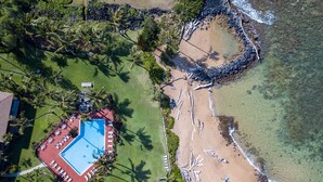 An aerial view of a resort with a swimming pool, beach, and palm trees. - Walkable to town and Oceanfront with A/C! (Kapaa)