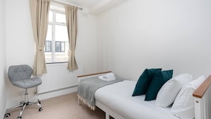 Une chambre à coucher avec un lit, une chaise, un radiateur et une fenêtre avec des rideaux.