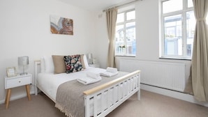 Une chambre à coucher avec un lit, des tables de chevet, un radiateur et une fenêtre avec des rideaux.