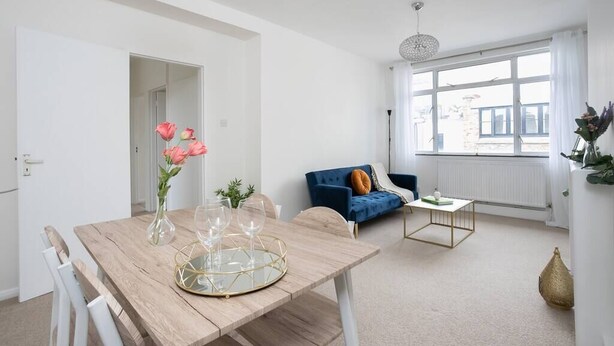 Un salon moderne avec une table à manger en bois, un canapé bleu et une grande fenêtre.