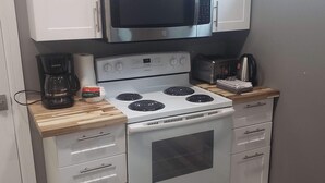 A compact kitchen with white cabinets, a stainless steel microwave, a white stove, and a coffee maker.