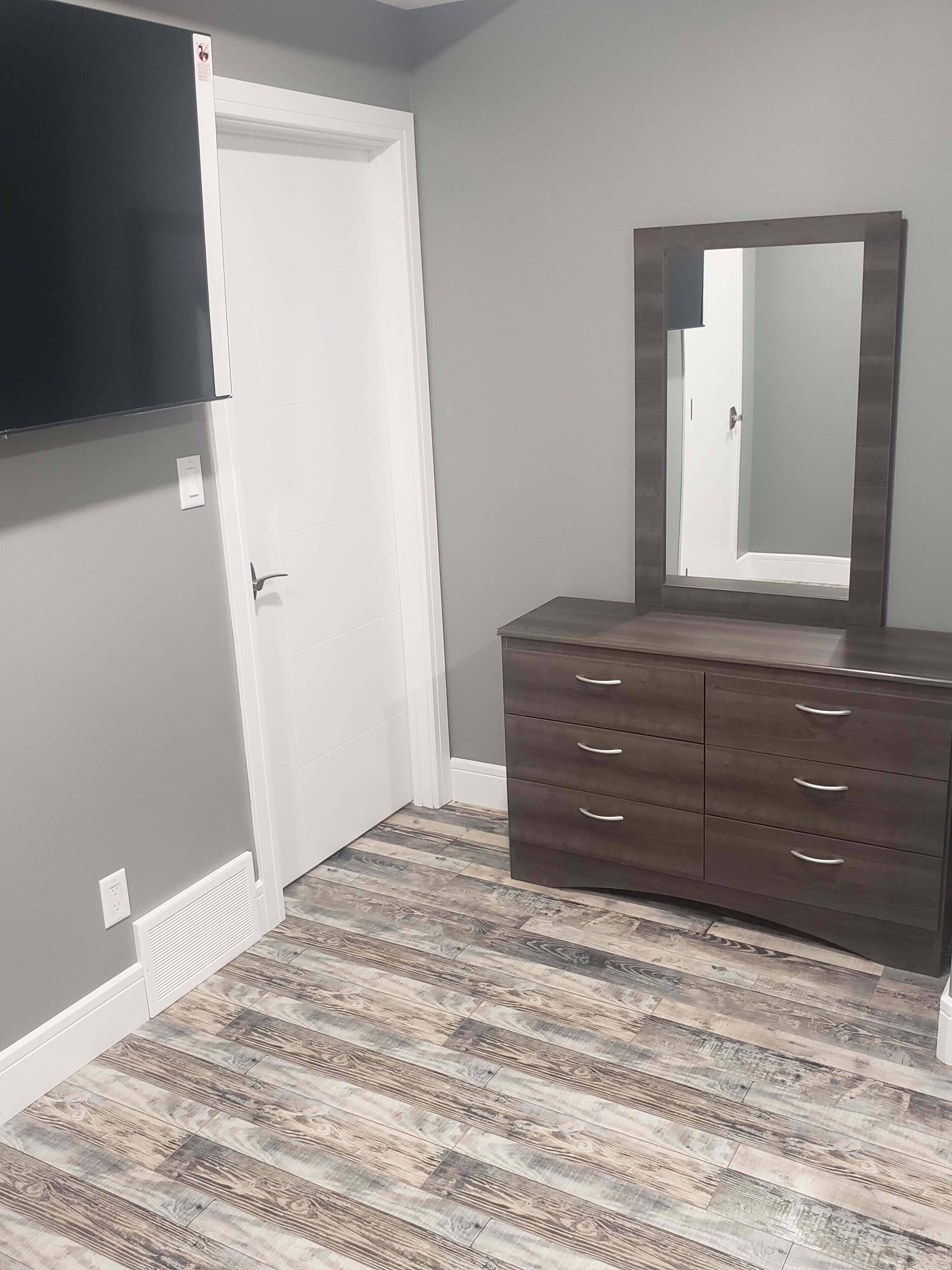 Een slaapkamer met een dressoir, een aan de muur bevestigde televisie, en een deur.